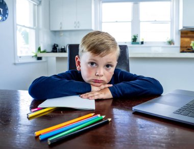 Coronavirus salgını. Kilitlenme ve okul kapanması. Yüz maskeli okul çocuğu evde sıkılmış ve depresif hissederek online eğitim dersleri izliyor. COVID-19 salgını çocukları çevrimiçi öğrenmeye zorluyor.