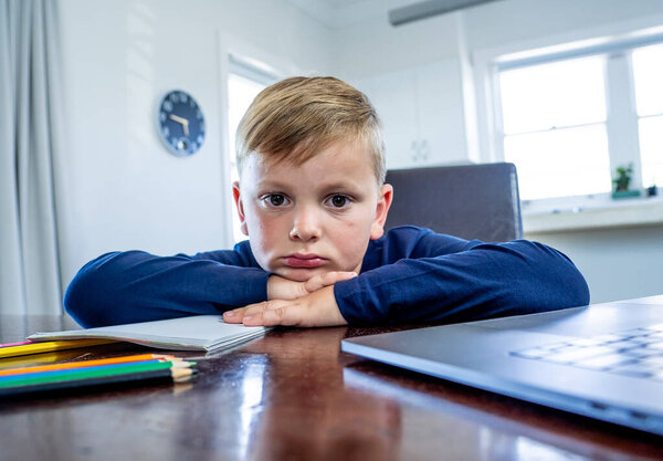 Coronavirus Outbreak. Lockdown and school closures. School boy with face mask watching online education classes feeling bored and depressed at home. COVID-19 pandemic forces children online learning.