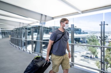 Coronavirus outbreak travel ban and restrictions. Traveler man with face mask at international airport affected by flight cancellation. COVID-19 pandemic and worldwide borders closures and shutdowns. clipart