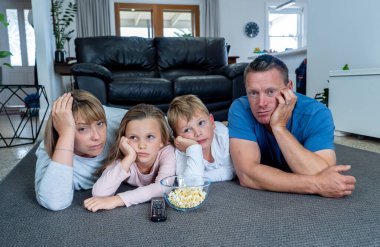 Coronavirus kilidi. Karantina COVID 19 salgını sırasında evde yalnız başına televizyon seyreden sıkıcı aile. Zorunlu tecrit ve kişisel tecrit önerileri aileleri evde kalmaya zorluyor.