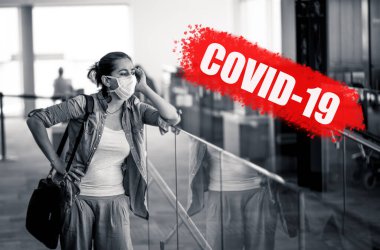 COVID-19 salgını. Havaalanındaki yüz maskeli gezgin kadın Coronavirus salgını ve dünya çapında sınırların kapatılması ve kapanması nedeniyle uçuş iptalinden etkilendi. Kırmızı ile yazılmış COVID-19.