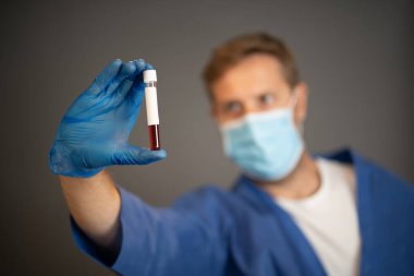 COVID-19. PPE 'deki doktor ya da laboratuvar teknisyeni. Kişisel koruyucu ekipman. Hastanedeki hastadan alınan kan örneği tüpünü tutuyor. Antikor ve aşı araştırmaları için Coronavirus kan testi.