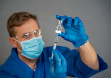 COVID-19 Coronavirus aşısı. Sars-CoV-2 virüsünü inceleyen şırıngalı bir bilim adamı aşı araştırması için klinik deneylere hazır. Erkek araştırmacı laboratuvarda potansiyel aşıyı test ediyor..