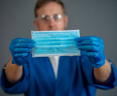 COVID-19. Doktor ya da hemşire yüz maskesi tutuyor. Virüsün yayılmasını engelleyin, kendinizi ve diğerlerini koruyun ve hasta bakımı ve sağlık görevlilerinin güvenliği için gerekli malzeme ve ekipman sağlanmasına yardım edin..