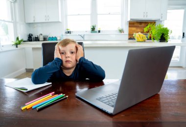 Coronavirus salgını. Kilitlenme ve okul kapanması. Yüz maskeli okul çocuğu evde sıkılmış ve depresif hissederek online eğitim dersleri izliyor. COVID-19 salgını çocukları çevrimiçi öğrenmeye zorluyor.