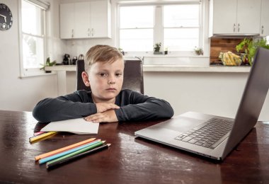 Coronavirus salgını. Kilitlenme ve okul kapanması. Yüz maskeli okul çocuğu evde sıkılmış ve depresif hissederek online eğitim dersleri izliyor. COVID-19 salgını çocukları çevrimiçi öğrenmeye zorluyor.