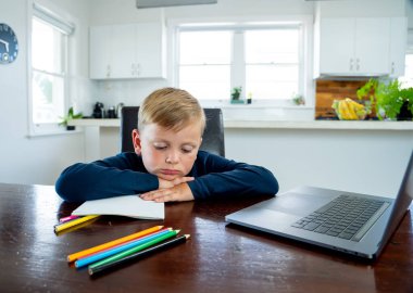 Coronavirus salgını. Kilitlenme ve okul kapanması. Yüz maskeli okul çocuğu evde sıkılmış ve depresif hissederek online eğitim dersleri izliyor. COVID-19 salgını çocukları çevrimiçi öğrenmeye zorluyor.