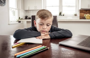 Coronavirus salgını. Kilitlenme ve okul kapanması. Yüz maskeli okul çocuğu evde sıkılmış ve depresif hissederek online eğitim dersleri izliyor. COVID-19 salgını çocukları çevrimiçi öğrenmeye zorluyor.