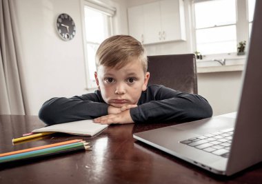 Coronavirus salgını. Kilitlenme ve okul kapanması. Yüz maskeli okul çocuğu evde sıkılmış ve depresif hissederek online eğitim dersleri izliyor. COVID-19 salgını çocukları çevrimiçi öğrenmeye zorluyor.