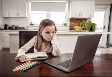 Coronavirus salgını. Kilitlenme ve okul kapanması. Yüz maskeli liseli kız çevrimiçi eğitim dersleri izlerken evde sıkılmış ve depresif hissediyor. COVID-19 salgını çocukları çevrimiçi öğrenmeye zorluyor.