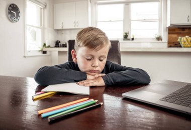 Coronavirus salgını. Kilitlenme ve okul kapanması. Yüz maskeli okul çocuğu evde sıkılmış ve depresif hissederek online eğitim dersleri izliyor. COVID-19 salgını çocukları çevrimiçi öğrenmeye zorluyor.