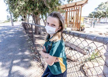 Covid-19 salgın okulları kapanıyor. Üzgün ve sıkılmış maskeli liseli kız kapalı okulunun dışında kendini depresif ve yalnız hissediyordu. Coronavirus önleme tedbirleri olarak kısıtlamalar ve tecrit.