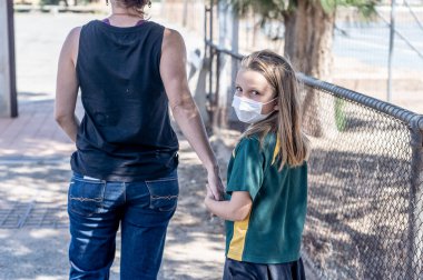 Covid-19 salgın okulları kapanıyor. Annem okul kapanırken okul maskeli Sad Schoolgirl 'ü alacak. Coronavirus salgını önleme tedbirleri olarak kısıtlamalar, karantina ve tecrit.