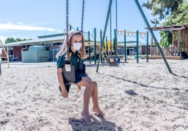 Covid-19 salgın okulları kapanıyor. Okul kapalıyken okul bahçesinde depresif ve yalnız hissetmekten sıkılmış maskeli kız öğrenci. Coronavirus önleme tedbirleri olarak kısıtlamalar ve tecrit.