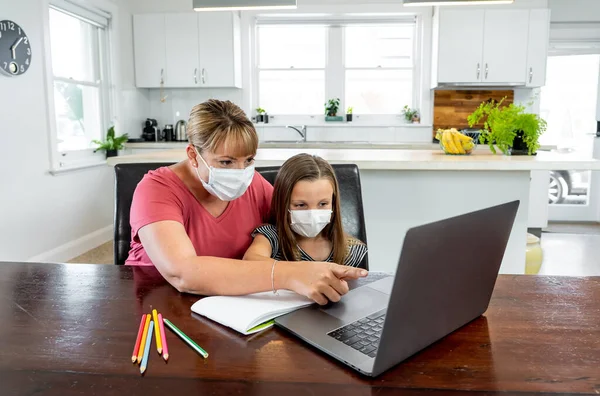 Coronavirus Outbreak. Lockdown and school closures. Mother helping bored daughter with face mask studying online classes at home. COVID-19 pandemic forces children and teachers online learning.