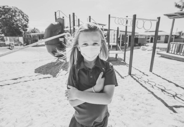 Covid-19 outbreak schools closures. Sad Schoolgirl with face mask bored feeling depressed and lonely in empty playground as school is closed. Restrictions and lockdown as Coronavirus containment measures.
