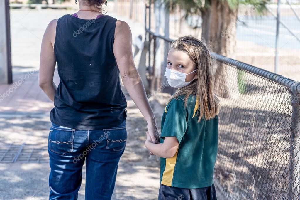 Covid-19 outbreak schools closures. Mum picking up Sad Schoolgirl with face mask as school is closed. Restrictions, quarantine and lockdown as Coronavirus pandemic containment measures.