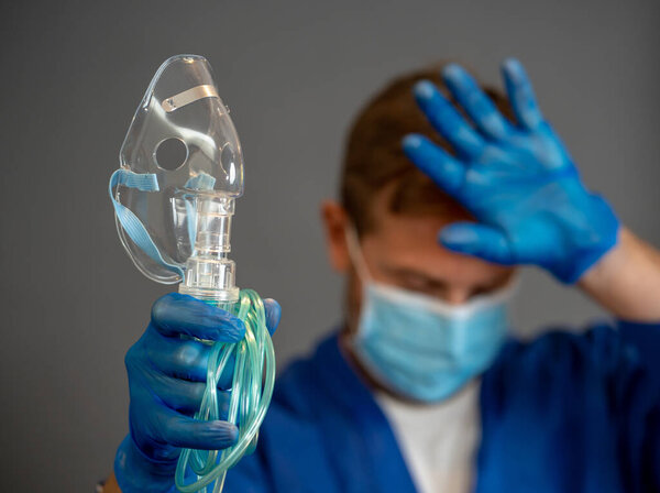 COVID-19 Outbreak. Exhausted Doctor holding non- invasive ventilator. Medical treatment and lack of equipment for coronavirus infected patients with SARS. Shortage of medical ventilators in hospitals.