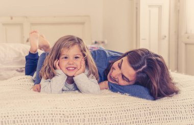 COVID-19 Salgını. Mutlu bekar anne-baba kadın ve küçük kız yalnızlık sırasında yatakta birlikte oynuyorlar. Anne ve küçük tatlı kız evde kalma kampanyası konseptinde yalnızlık çekiyor..