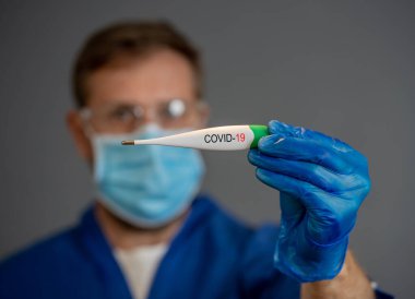 COVID-19 Salgını. Doktor termometreyi tutuyor. Kendini koru ve koronavirüsün yayılmasını engelle. Semptomlar, ateş, öksürük ve nefes almakta güçlük çekiyorsanız, tıbbi yardım isteyin..