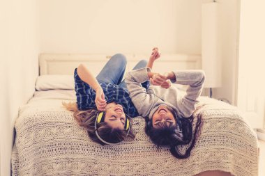 COVID-19 tecrit. Kendinden emin ve iyimser kadınlar en iyi kız arkadaşlar gülerek çevrimiçi müzik dinliyorlar evde yalnızken yatakta şarkı söyleyip dans ediyorlar. Evde güvenli sağlık ve güvenlik kampanyası yapın..