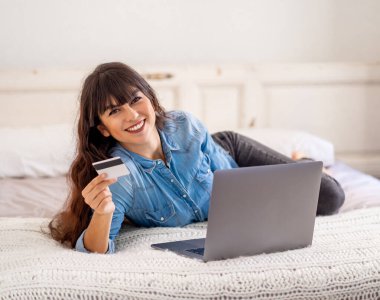 COVID-19 Salgını. Kapatma ve online alışveriş. Kredi kartıyla çekici genç bir kadın dizüstü bilgisayar kullanarak Coronavirus kilitleme ve sosyal uzaklık süresince evdeki internetten yemek alıyor..