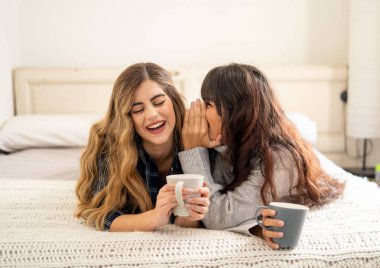 COVID-19 tecrit. Kendinden emin ve iyimser kadınlar en iyi kız arkadaşlar yatakta konuşurken ve gülerken sıcak içecekler evde yalnızken. Evde kal. Sağlığını ve güvenliğini koru..