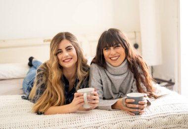 COVID-19 tecrit. Kendinden emin ve iyimser kadınlar en iyi kız arkadaşlar yatakta konuşurken ve gülerken sıcak içecekler evde yalnızken. Evde kal. Sağlığını ve güvenliğini koru..