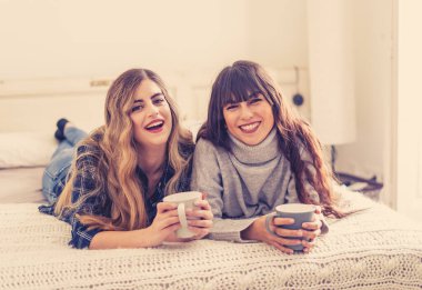 COVID-19 tecrit. Kendinden emin ve iyimser kadınlar en iyi kız arkadaşlar yatakta konuşurken ve gülerken sıcak içecekler evde yalnızken. Evde kal. Sağlığını ve güvenliğini koru..