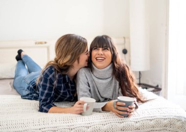 COVID-19 tecrit. Kendinden emin ve iyimser kadınlar en iyi kız arkadaşlar yatakta konuşurken ve gülerken sıcak içecekler evde yalnızken. Evde kal. Sağlığını ve güvenliğini koru..
