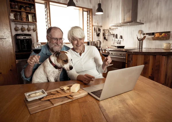 COVID-19 Stay connected. Happy senior couple with pet dog and wine video calling friends on laptop or online chatting with family celebrating easing of coronavirus restrictions lockdown. Hope concept.