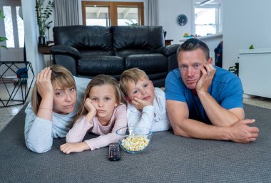 Coronavirus kilidi. Karantina COVID 19 salgını sırasında evde yalnız başına televizyon seyreden sıkıcı aile. Zorunlu tecrit ve kişisel tecrit önerileri aileleri evde kalmaya zorluyor.
