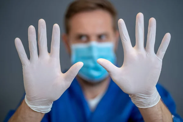 COVID-19 Outbreak. Help to stop the virus spread. Male Doctor or nurse wearing face surgical mask and gloves PPE showing hands in STOP gesture. Stay safe, Protect yourself protect others coronavirus campaign.