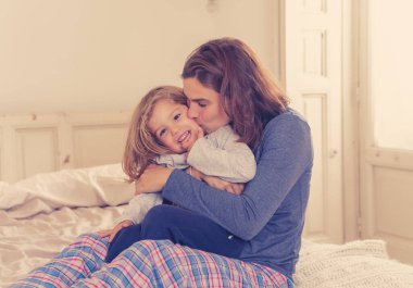 COVID-19 Salgını. Mutlu bekar anne-baba kadın ve küçük kız yalnızlık sırasında yatakta birlikte oynuyorlar. Anne ve küçük tatlı kız evde kalma kampanyası konseptinde yalnızlık çekiyor..