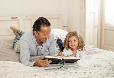 COVID-19 tecrit. Baba ve küçük kız birlikte kitap okuyorlar. Mutlu baba ve küçük kız karantinada yatakta masal okurken eğleniyorlar. Evde kal, güvende ol ve evde eğitim al..