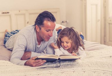 COVID-19 tecrit. Baba ve küçük kız birlikte kitap okuyorlar. Mutlu baba ve küçük kız karantinada yatakta masal okurken eğleniyorlar. Evde kal, güvende ol ve evde eğitim al..