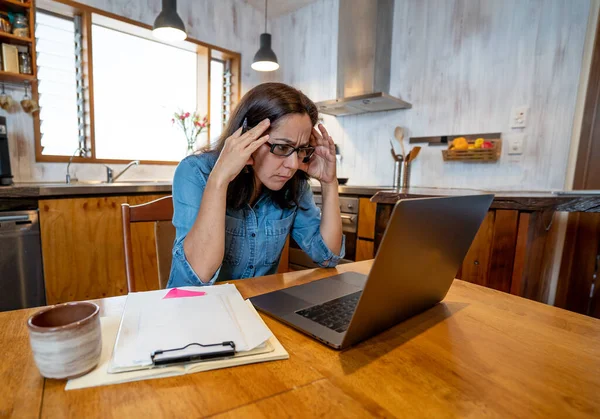 Stressed business woman working from home on laptop looking worried, tired and overwhelmed. Exhausted female working remotely during social distancing. Mental health and coronavirus lockdown.