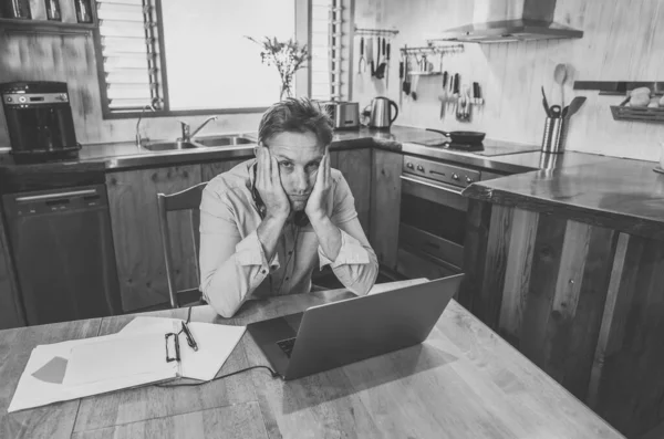 Stressed business man on laptop working from home looking worried, tired and overwhelmed. Exhausted entrepreneur working remotely during social distancing. Mental health and coronavirus lockdown.