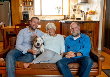 Family of adult man and senior parents relaxing loving their cute pet dog enjoying time together relaxing on the sofa. Positive image of life at home and new normal after coronavirus Outbreak. clipart