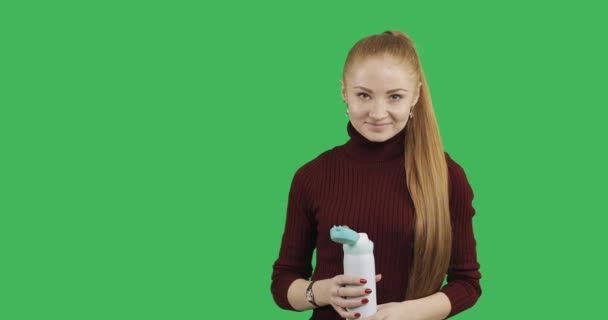 緑の背景の魔法瓶からホットド リンクを飲んでいる女性 — ストック動画