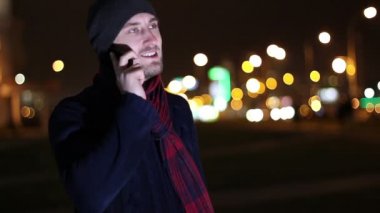 Yakışıklı ciddi genç adam cep telefonuyla konuşuyor. Gece açık renkli.