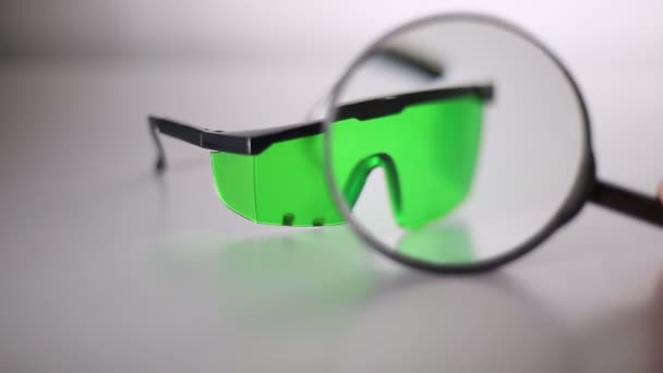 レーザー保護メガネはテーブルの上です 緑色のレーザー安全メガネのクローズ アップ レーザー放射からの損傷します レーザー治療後のスポット 虫眼鏡の画像 — ストック動画