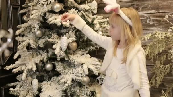 ウサギの白い衣装で小さな女の子がクリスマス ツリーを飾る — ストック動画