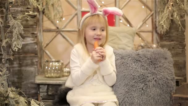 ウサギの白装束の女の赤ちゃんのクリスマスの装飾の中でニンジンを食べる — ストック動画