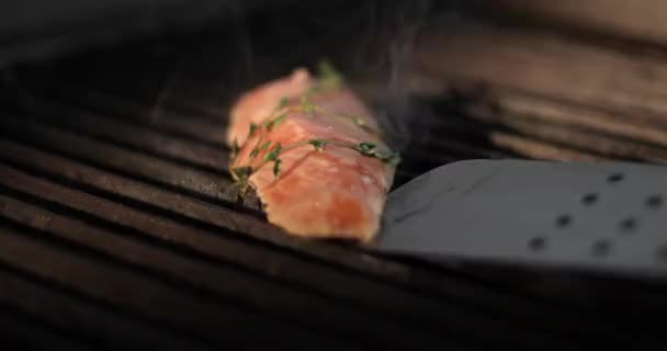 Koch dreht mit einer Metallzange ein Stück frisches rotes Fischfilet auf einem Elektrogrill. — Stockvideo