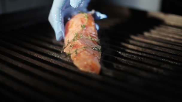 Cooks hand i handske sätter en bit färsk röd fiskfilé på en elgrill. Röken stiger.. — Stockvideo