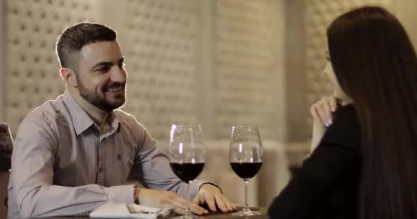 Mujer morena y hombre barbudo están sentados a la mesa en el restaurante y beber vino tinto . — Vídeo de stock