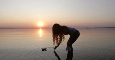 Young woman dreaming during sunset launch a few paper boats.