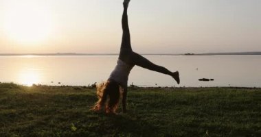 Redhead girl has fun on the green grass making an acrobatic wheel.