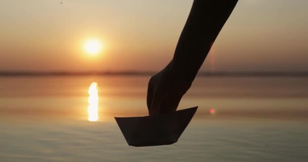 Silhouette einer menschlichen Hand, die ein Papierboot im Wasser des Meeres oder Sees bei Sonnenuntergang loslässt. Nein. — Stockvideo